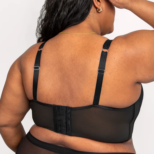 Person wearing a black sheer top with thin straps on a plain background